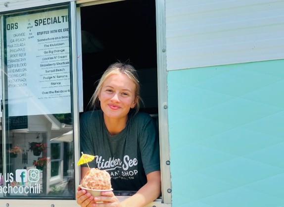 A smiling server handing a shave ice out of the camper's serving window